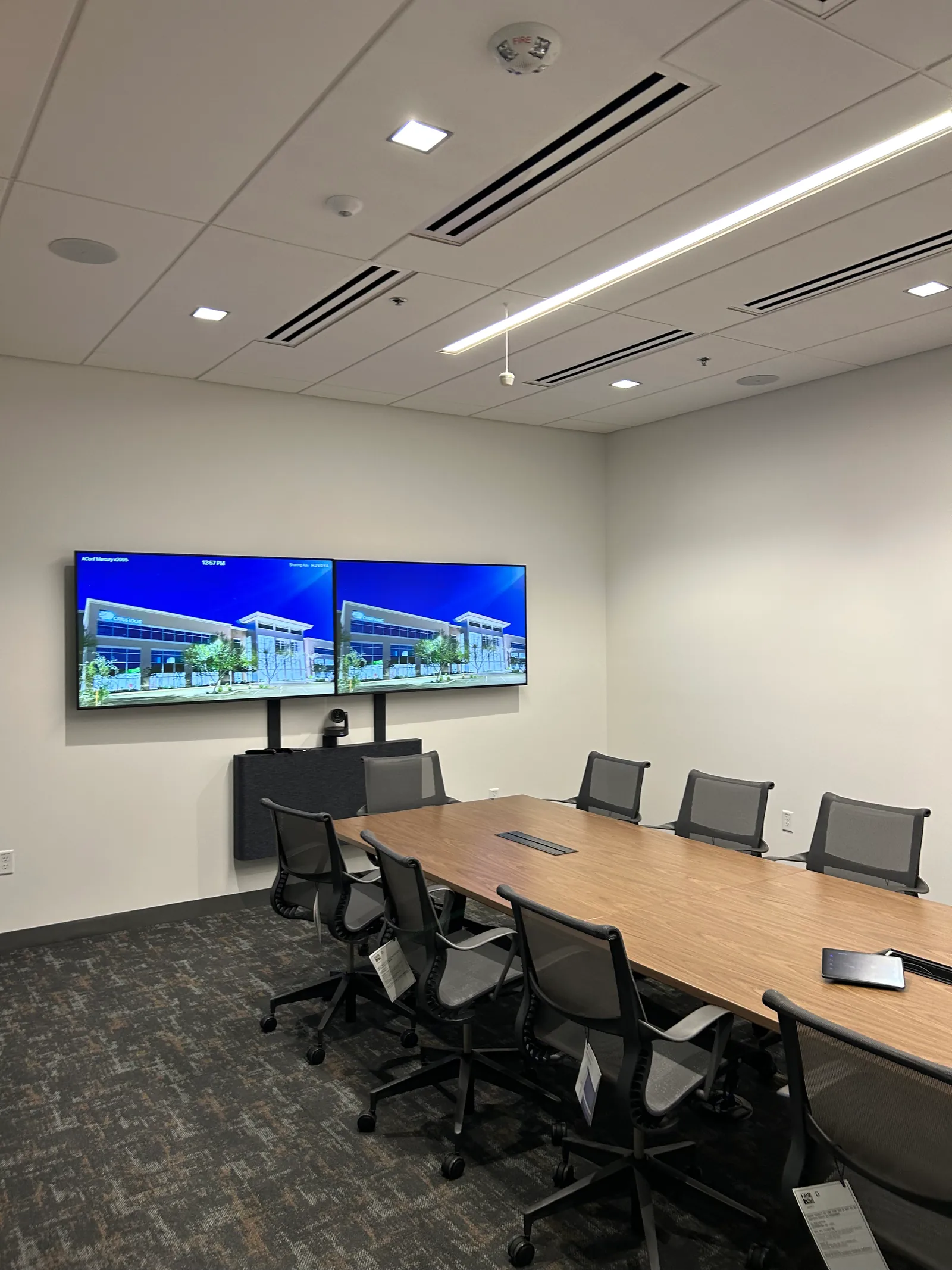 Meeting room with a long table, office chairs and wall-mounted displays.