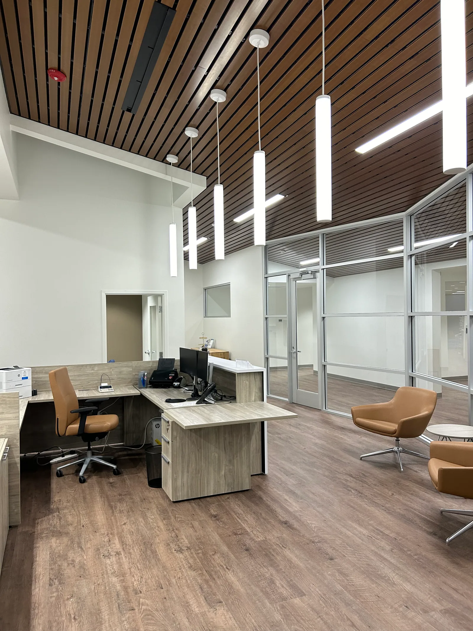 Desk area beside waiting chairs, glass partitions and a timber-slat ceiling.