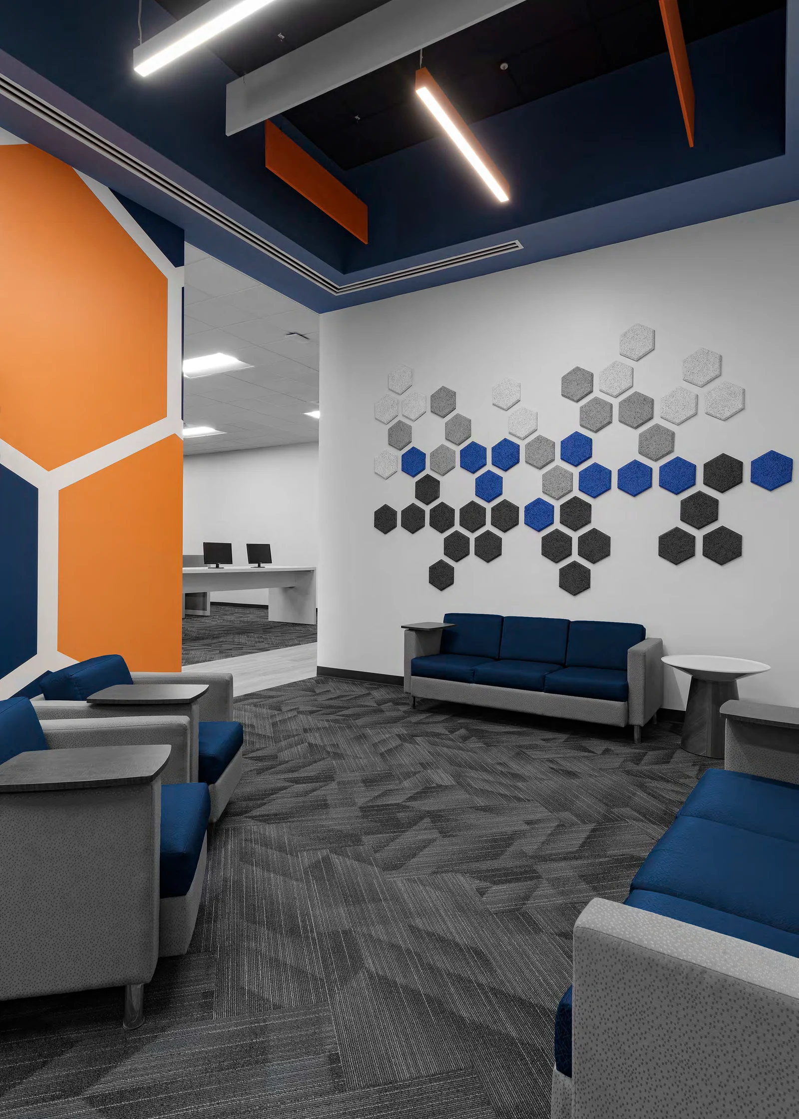 Quiet lounge with blue seating and a hexagonal wall installation.