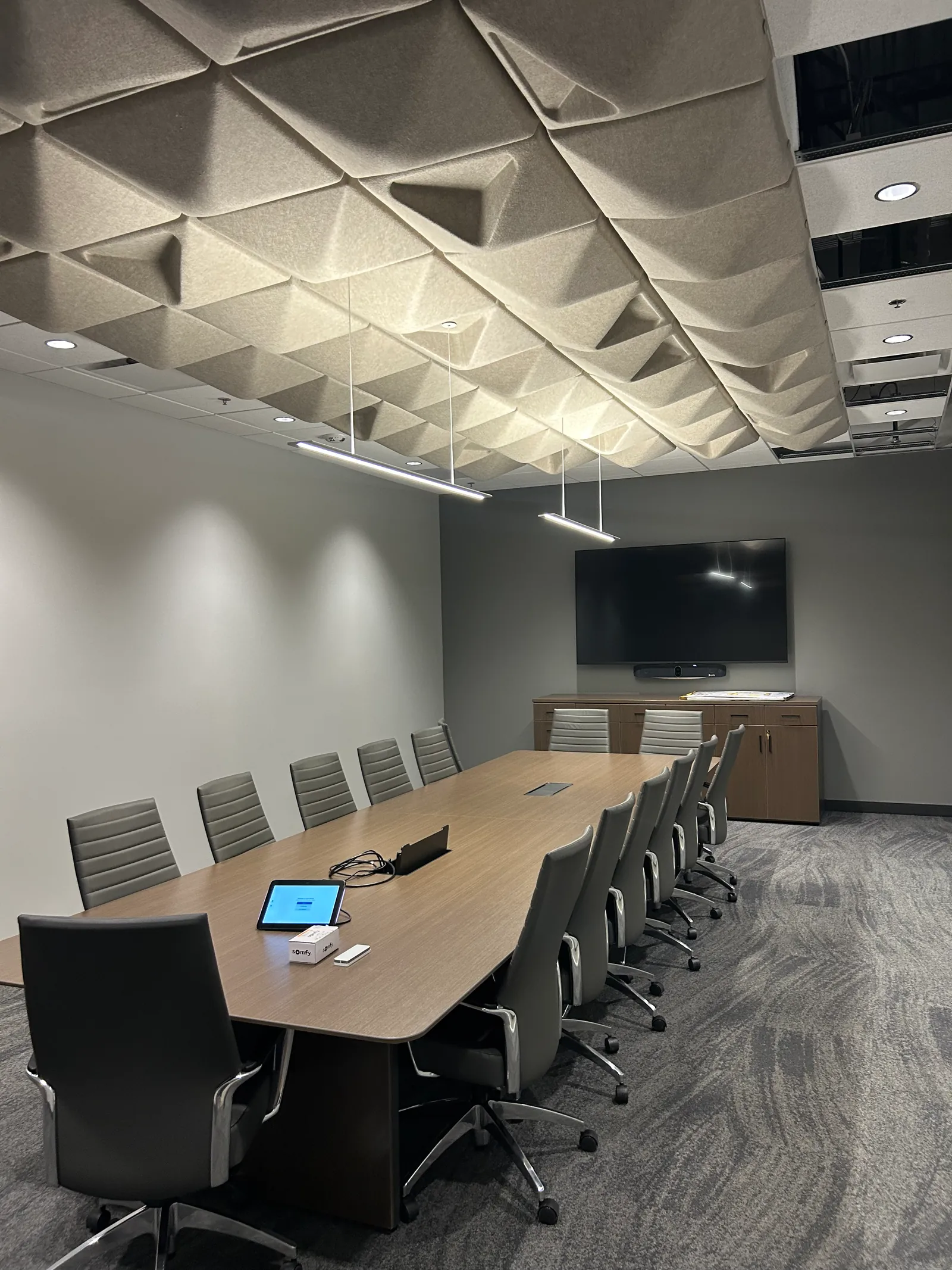 Boardroom with a long timber table, acoustic ceiling panels and a wall-mounted display.