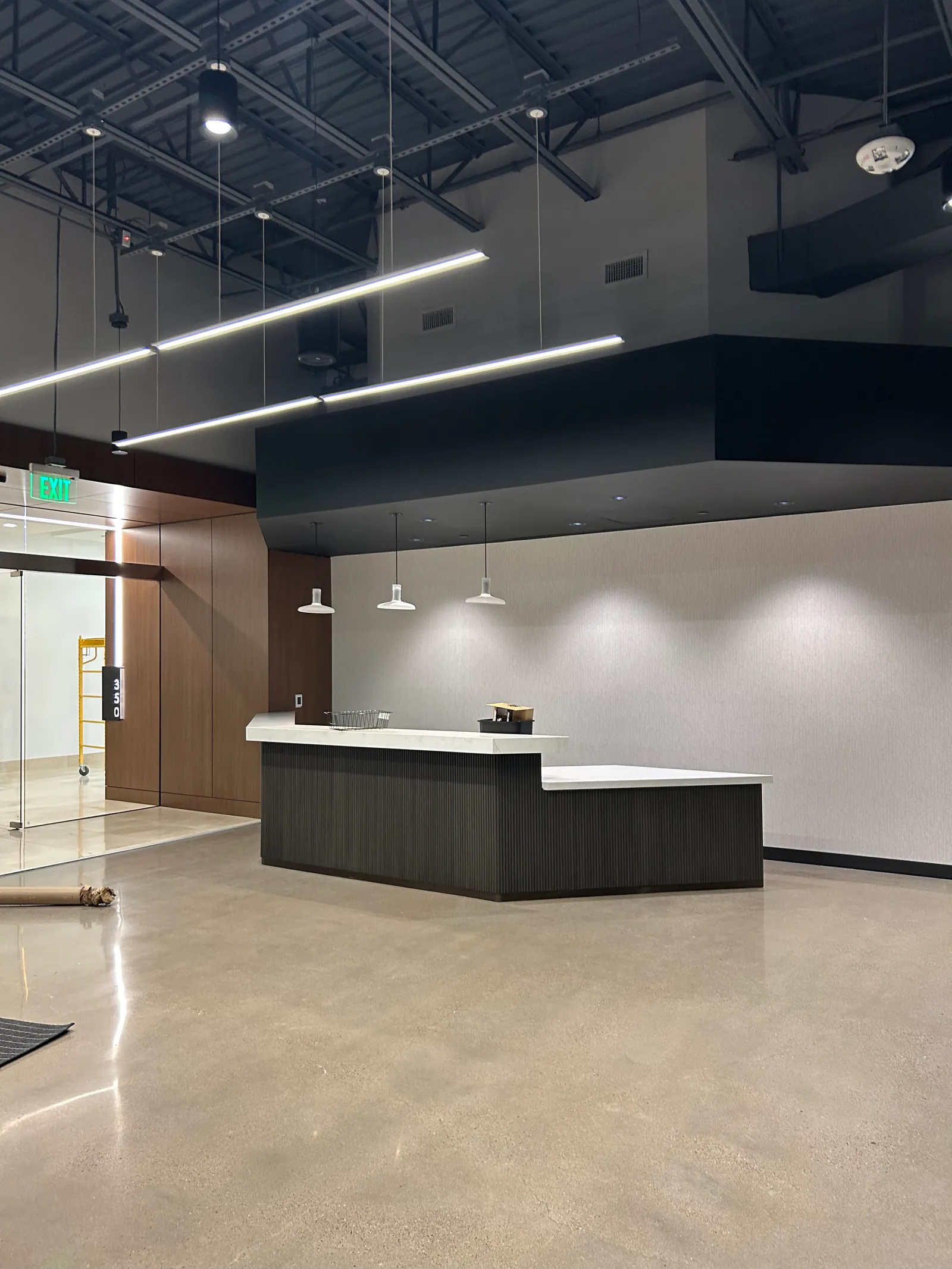 Reception counter beneath an exposed ceiling with suspended linear lighting.