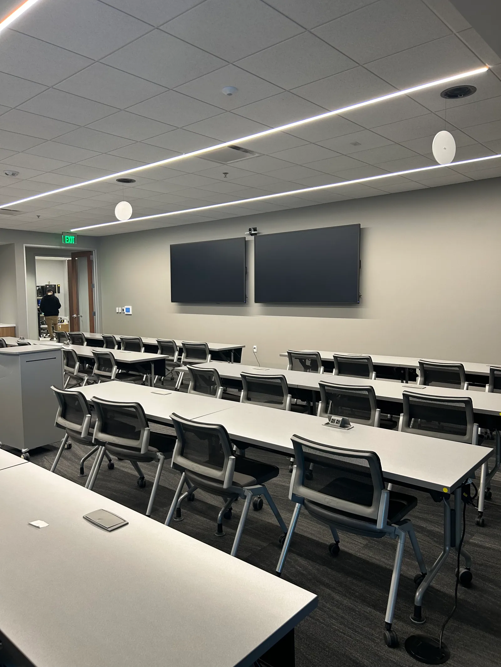 Training room with rows of tables and two wall-mounted displays.